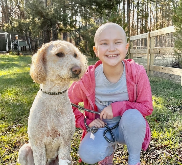 Olivia smiles and she sits with her dog outside.