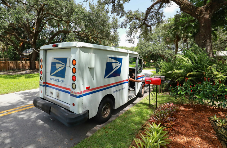 Fort Lauderdale, Florida, USA - September 3, 2020: Mailman delivering mail in a postal truck puts letters into a red mailbox.
